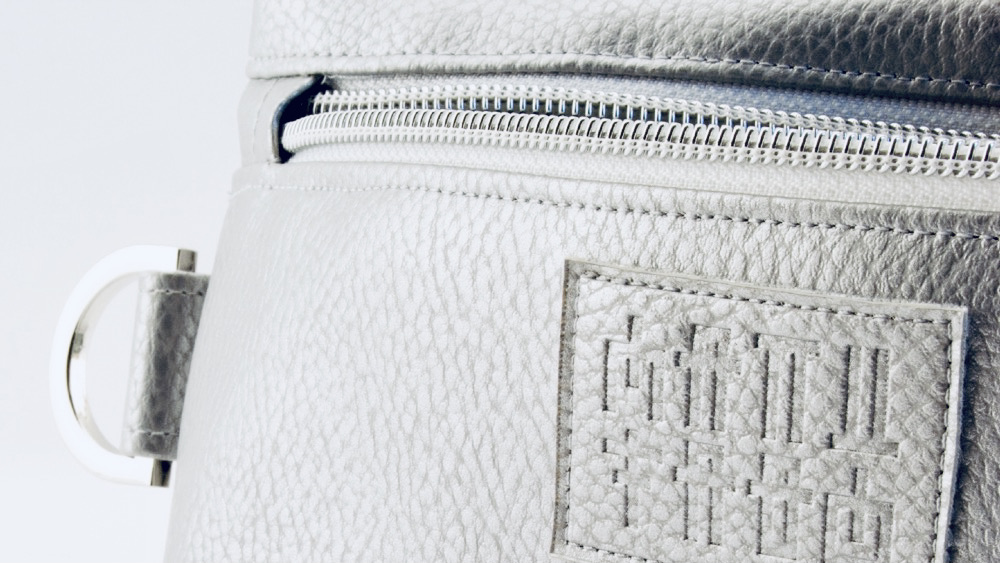 Close-up of Manufabo logo and hardware details on a metallic silver cosmetic bag