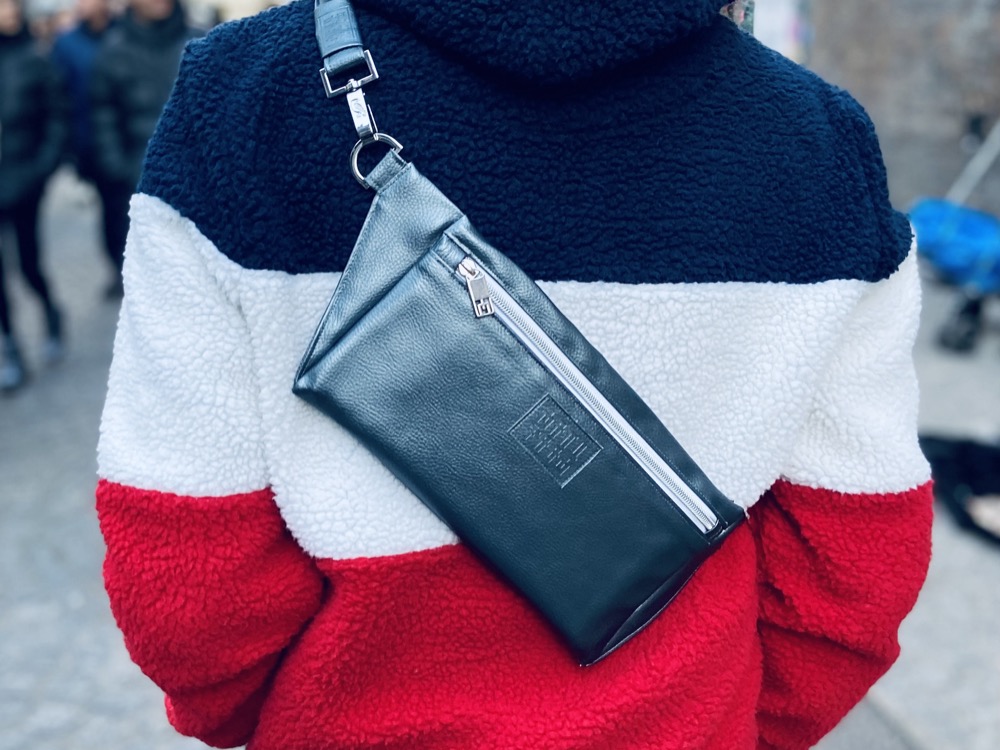 Man in London wearing a blue, white, and red striped plush hoodie with a Manufabo Metallic Slate Gray Belt Bag across his back