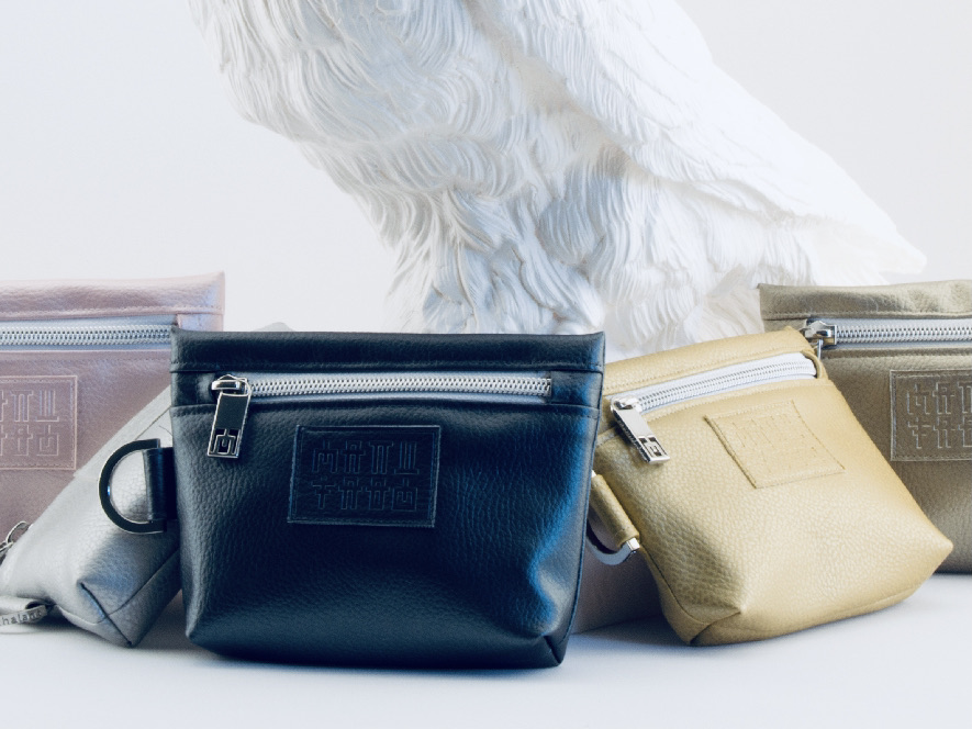 Manufabo Mini Bags in various metallic hues displayed in front of a white raven statue