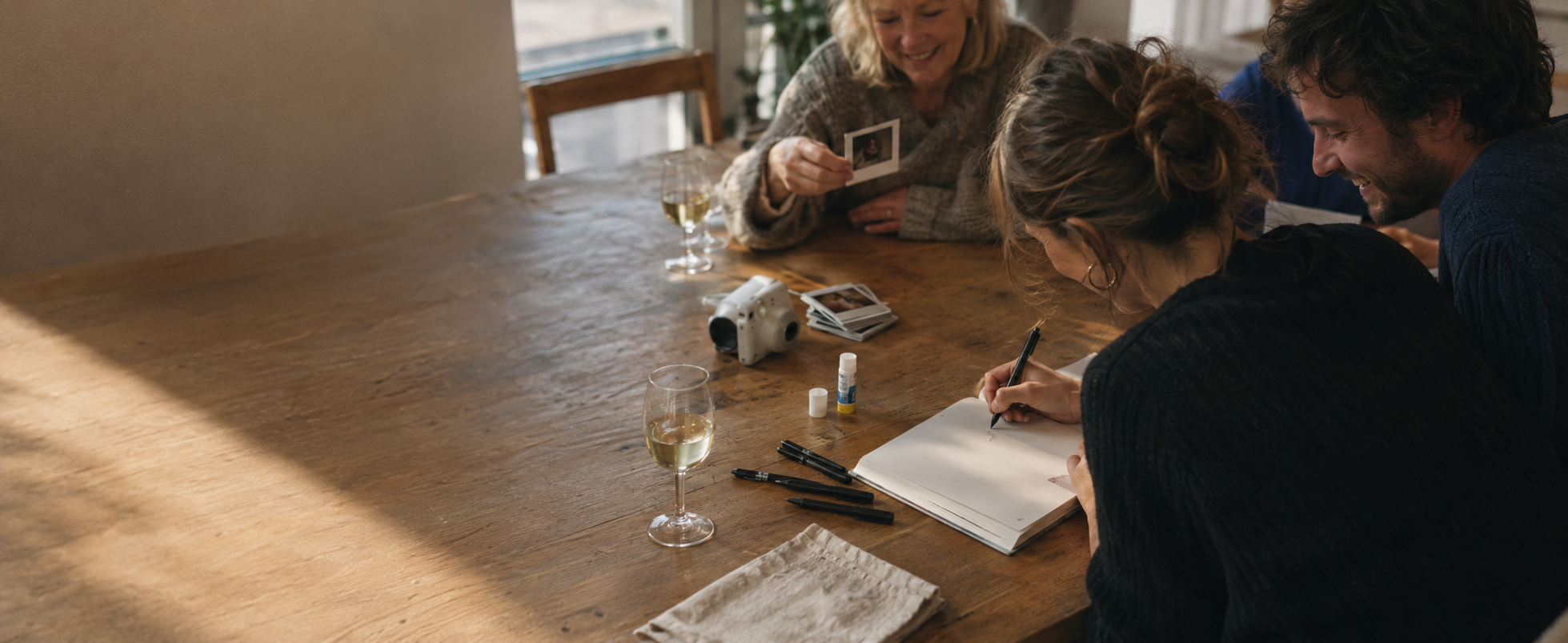MEMENTO guest book – three guests at a table writing their entries, with an instant camera and polaroids